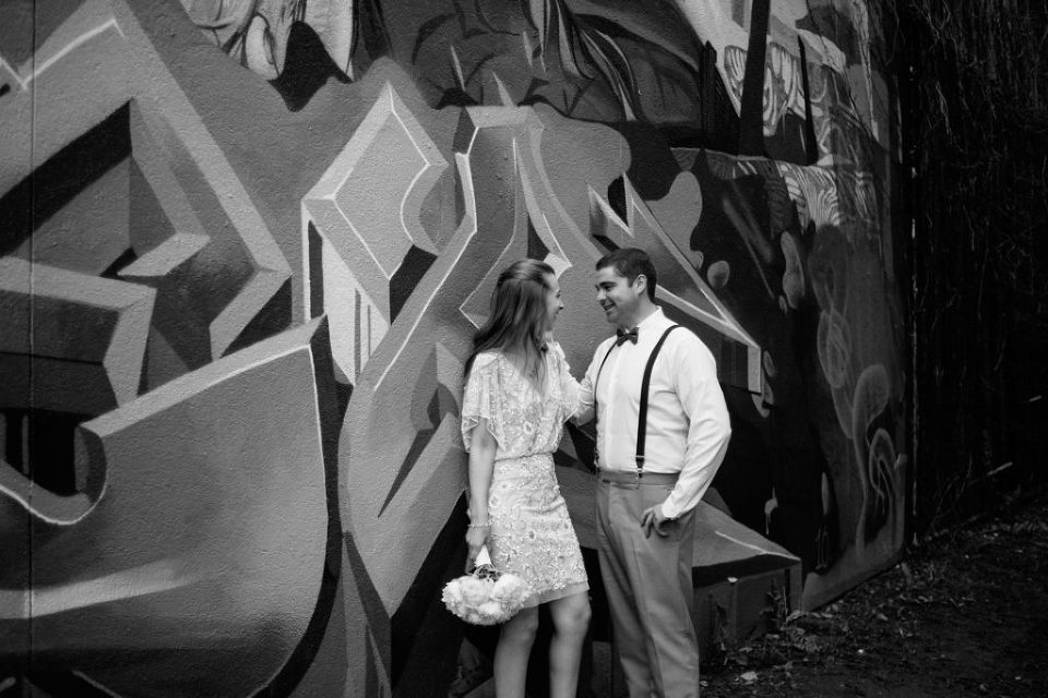 black and white photo of bride and groom leaning up against graffiti wall in Toronto, ontario