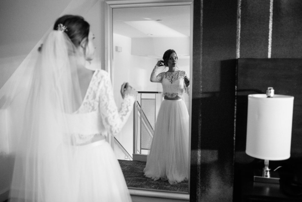 the bride looking in a mirror for the first time after putting on her two piece Sash and Bustle wedding dress in Toronto
