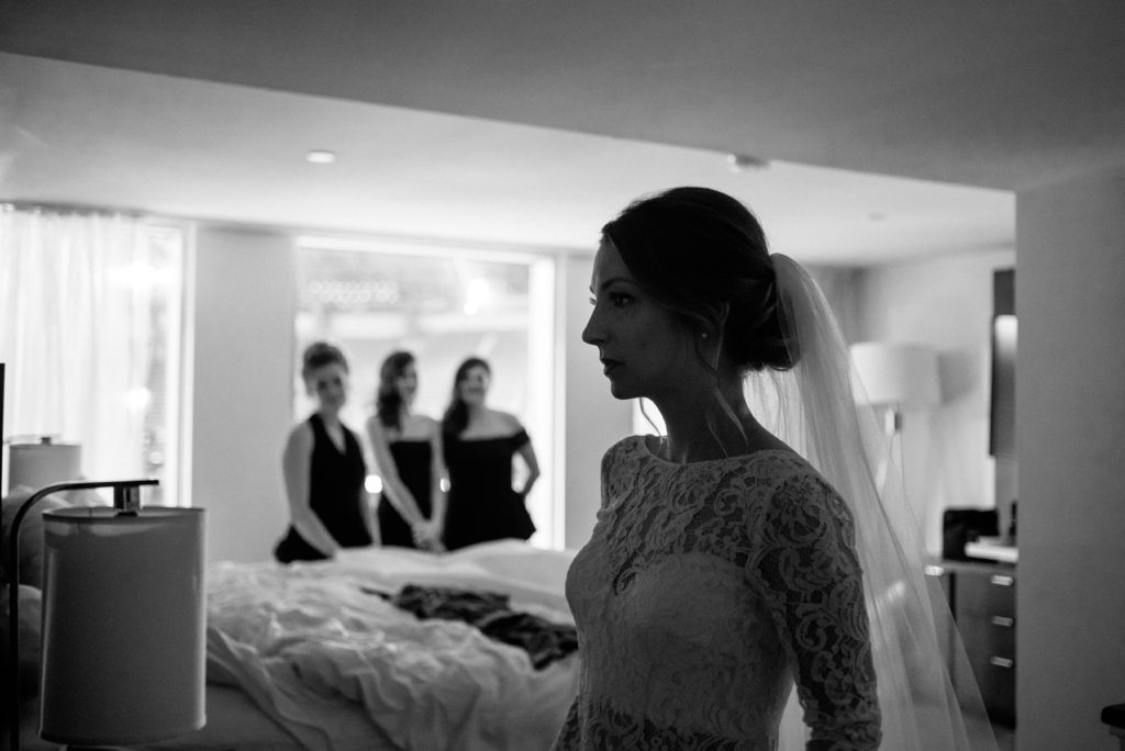bride looking at herself in the mirror and her bridesmaids are in the background 
