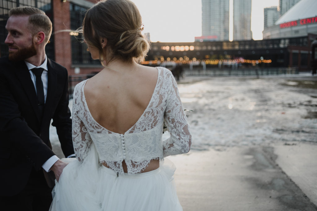 candid of bride and groom walking at sunset outside Steam Whistle Brewery in Toronto wearing a two piece Sash and Bustle wedding dress