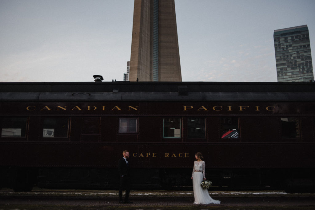 bride and groom posing infant of Canadian pacific train cart by the CN tower in Toronto