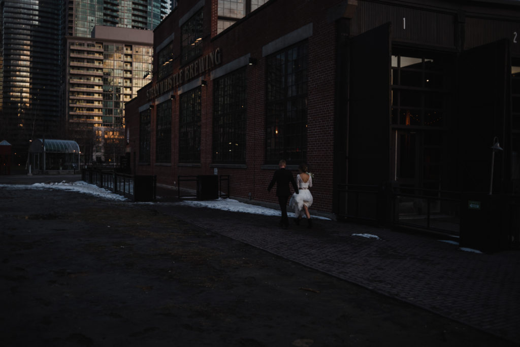 bride and groom walking towards entrance of steam whistle brewery in Toronto at sunset