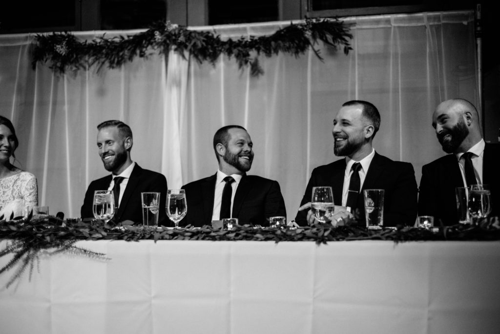 black and white photo of groomsmen laughing at the head table