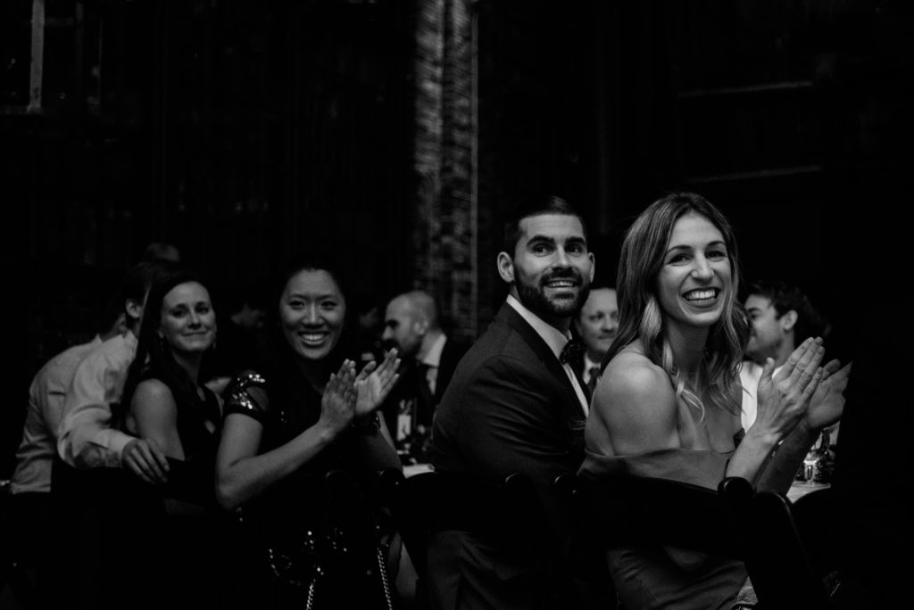 black and white photo of guests clapping after bride and grooms speech