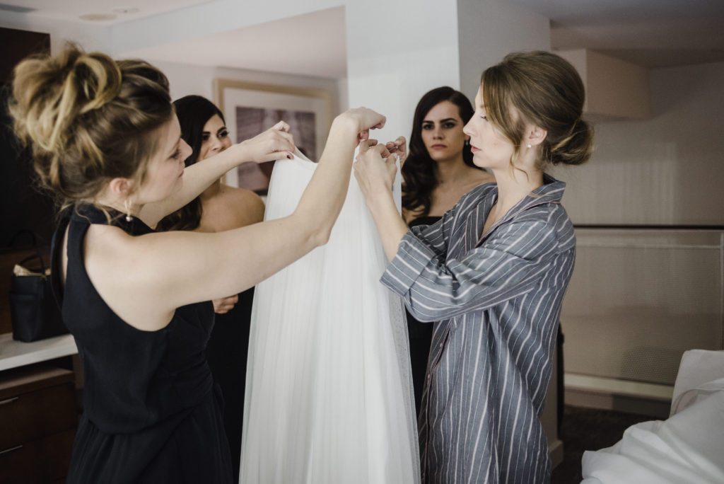 bride and bridesmaids holding up her wedding dress that she is about to put on