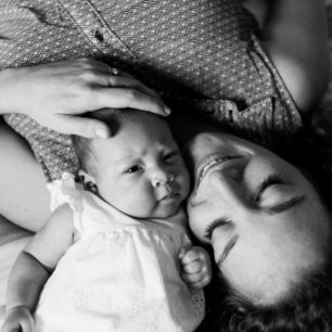 a close up black and white portrait of a mother and her newborn daughter. The photo is of the two of them laying side by side with their heads together
