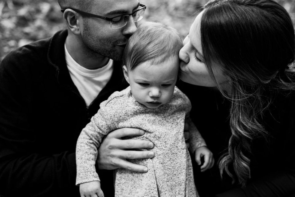 black and white family picture of a baby girl in the middle with mother and father on either side kissing her cheeks